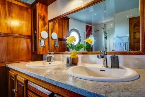 Salle de bains luxueuse avec double vasque aux Terrasses Du Volcan, mobilier en bois, plan de travail en granit et fleurs jaunes