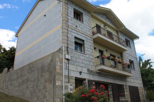 Edificio de hotel de piedra de tres pisos en Vigo, Zamora con balcones, flores y cielo azul despejado