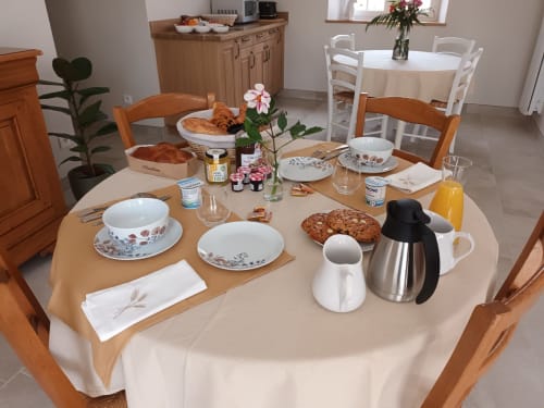 Table de petit-déjeuner élégante à La Vallee Joly B&B au Vast, France, avec viennoiseries, fleurs fraîches et couverts dressés.