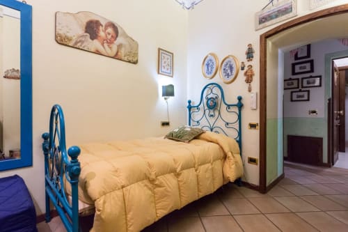 Letto in metallo blu con biancheria gialla nella Angel Room di Dormire Assisi B&B ad Assisi, Italia, con decorazioni murali