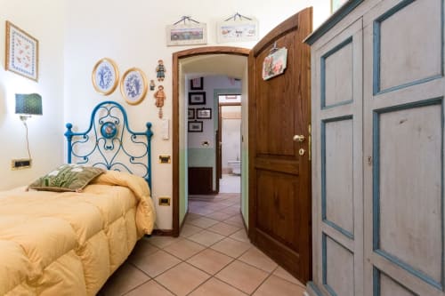 Accogliente camera da letto a Dormire Assisi B&B con letto in ferro battuto blu, porte in legno e pavimento in cotto.