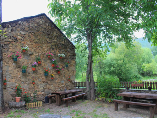 Cabaña de piedra con flores colgantes, mesas de picnic de madera y árbol en Turismo en Sanabria, Zamora