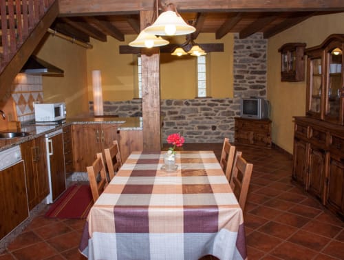 Comedor rústico del hotel Turismo en Sanabria en Zamora con vigas de madera, muros de piedra, mantel a cuadros y lámpara colgante