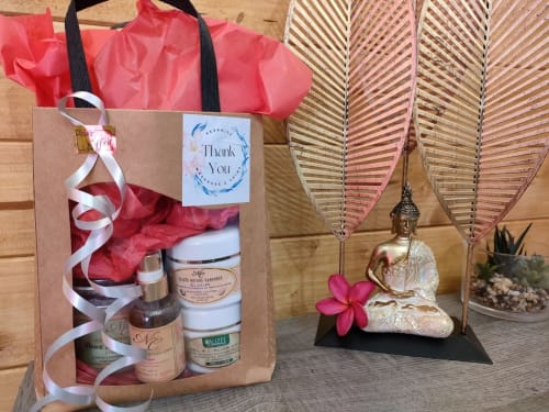 Coffret spa avec papier de soie rose, produits de soin, carte de remerciement, statue Bouddha et plumes décoratives à Résidence Les 2