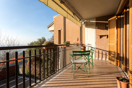 Sunny balcony at Dormire Assisi with green chairs, wooden deck, brick building, and scenic valley view in Assisi, Italy