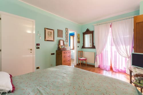 Bright mint-green bedroom at Dormire Assisi in Assisi, Italy, with floral bedding, pink curtains, wooden furniture, and