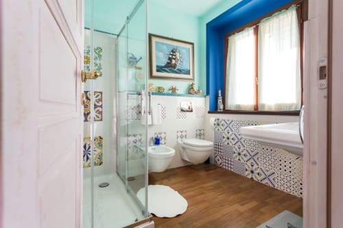 Modern bathroom at Dormire Assisi with walk-in shower, blue accents, decorative tiles, and garden views through window