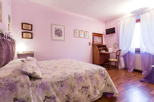 Camera da letto rosa presso Dormire Assisi B&B ad Assisi con biancheria floreale, scrivania in legno, TV e tende viola