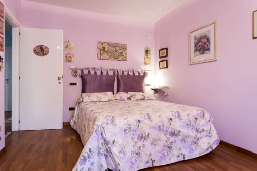 Pink bedroom at Dormire Assisi in Assisi with floral bedding, purple headboard, wall art, and wooden floors