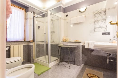 Modern bathroom at Dormire Assisi with glass shower enclosure, dual sinks, white fixtures, and heated towel rack in Assisi