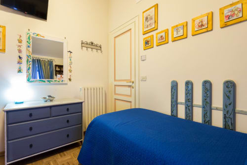 Camera accogliente al Dormire Assisi B&B con letto blu, cassettiera blu scuro e quadri colorati alle pareti