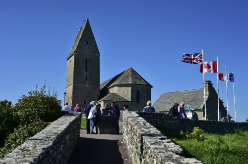 Église en pierre historique avec haut clocher à Le Vast, France, drapeau et murs de pierre