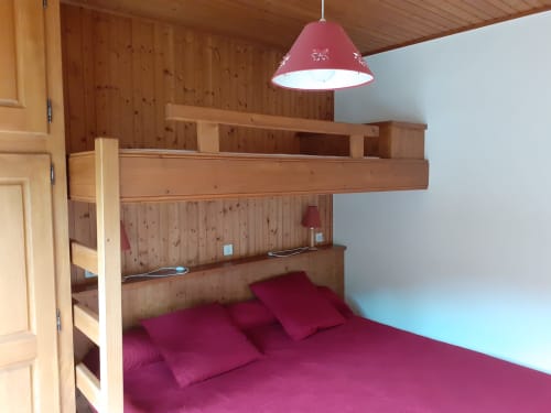Chambre douillette de chalet avec lit mezzanine, linge bordeaux, intérieur en bois et lampe suspendue aux Arcosses, La Giettaz
