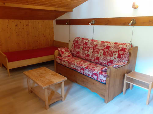 Confortable salon du chalet Les Arcosses avec canapé en bois, coussins rouges à motifs et décoration montagnarde