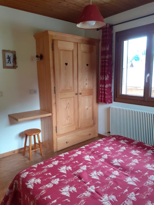 Chambre douillette du Chalet Les Arcosses à La Giettaz avec penderie en bois, literie rouge à motifs et vue sur les montagnes