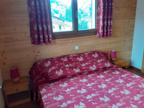 Chambre chaleureuse au Chalet Les Arcosses avec literie à motifs bordeaux, murs en bois, fenêtre avec vue montagne