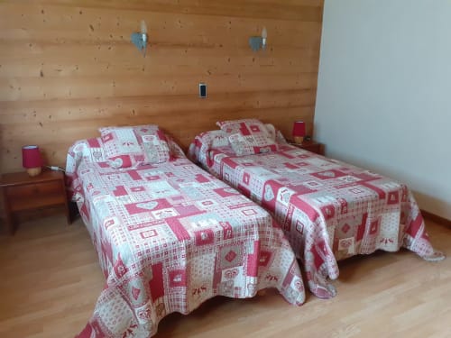 Deux lits jumeaux aux couettes rouges et blanches dans une chambre lambrisée du Chalet Les Arcosses, La Giettaz