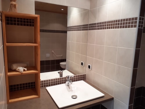 Salle de bain moderne au Chalet Les Arcosses avec douche carrelée, lavabo blanc et rangements en bois