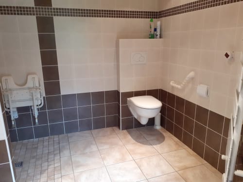 Salle de bains accessible en fauteuil roulant au Chalet Les Arcosses avec toilettes murales, barres d'appui et carrelage beige