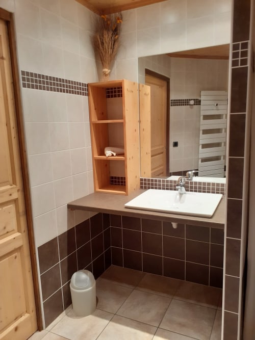 Salle de bain moderne du Chalet Les Arcosses avec lavabo blanc, miroir, carrelage foncé et rangements en bois