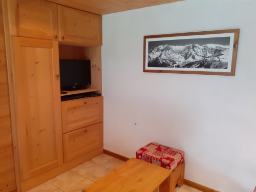 Chambre cosy du Chalet Les Arcosses avec mobilier en bois, télévision, photographie montagne et banc rouge aux coussins à La