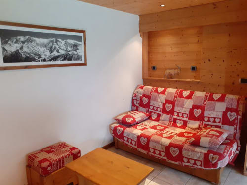 Appartement alpin douillet au Chalet Les Arcosses avec canapé à motifs cœurs rouges, murs en bois, tableaux montagnards et sol carrelé