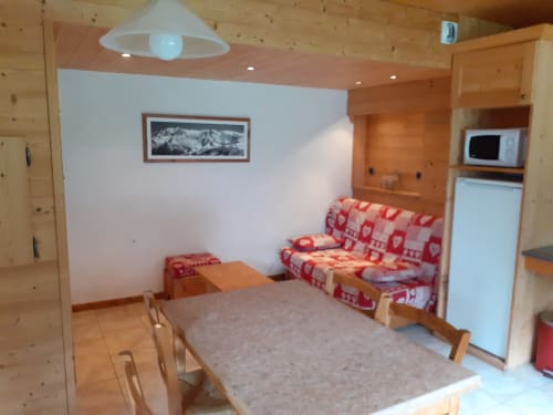 Petit appartement confortable du Chalet Les Arcosses à La Giettaz avec table à manger, canapé rouge à motifs, kitchenette et vue montagne