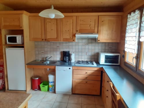 Cuisine en bois de l'appartement Chalet Les Arcosses avec cuisinière, réfrigérateur, micro-ondes et comptoir à La Giettaz