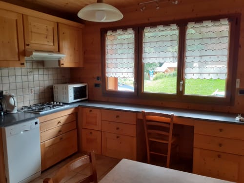 Cuisine en bois avec vue sur le jardin au Chalet Les Arcosses, La Giettaz. Équipée de poêle, micro-ondes et fenêtres donnant sur