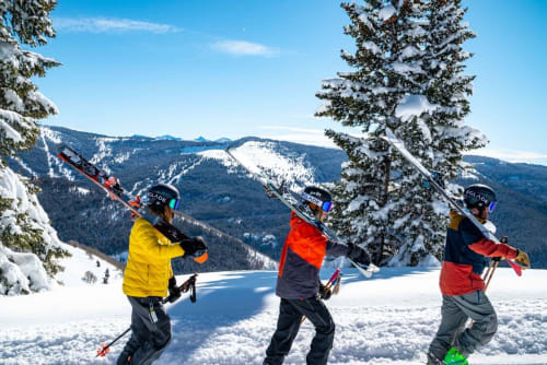 Trois skieurs profitent de la poudreuse près du Chalet Les Arcosses à La Giettaz, avec montagnes enneigées et lac gelé en arrière-plan