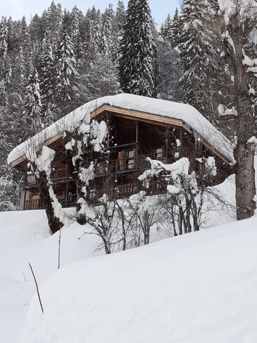 Chalet Les Arcosses, lodge en bois enneigé niché dans la forêt de La Giettaz, entouré de neige et de sapins