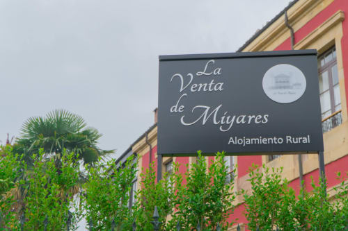 La Venta de Miyares hotel sign with 'Alojamiento Rural' text, colonial building facade behind, Piloña Spain