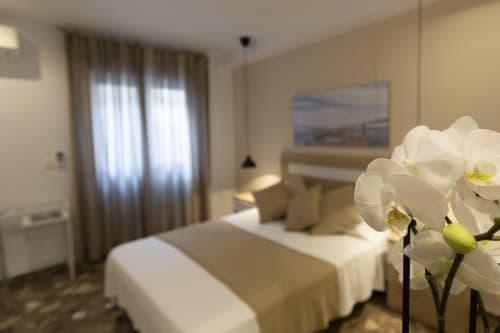 Habitación moderna del Room Boutique 32 en Denia con orquídeas blancas, cama con ropa de cama beige y luz natural del balcón