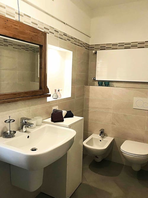 Modern bathroom in Ca Cortigiane Venice apartment with white sink, bidet, toilet, and wooden-framed mirror