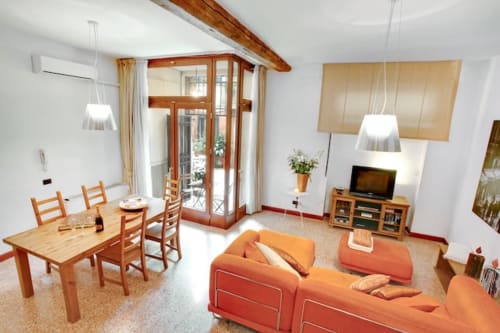 Ca Cortigiane Suite a Venezia: soggiorno moderno con divano arancione, tavolo da pranzo, TV, lampade a sospensione e accesso alla terrazza