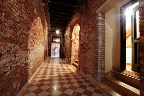 Storico corridoio in mattoni della Ca Cortigiane di Venezia con pavimento a scacchiera e archetti in pietra
