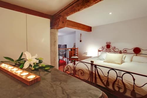 Camera della Ca Cortigiane a Venezia con letto in ferro battuto, travi in legno, candele e vista sulla città
