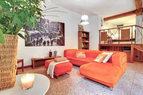 Soggiorno di un appartamento moderno a Venezia con divano componibile rosso-arancione, lampada a sospensione, opere d'arte e arredi in legno a Ca