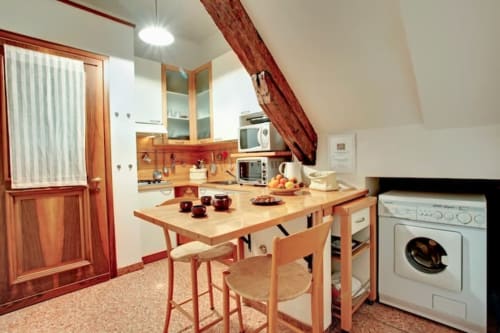 Cucina della Ca Cortigiane Suite con tavolo da pranzo, lavatrice, fornello e travi in legno nell'appartamento veneziano