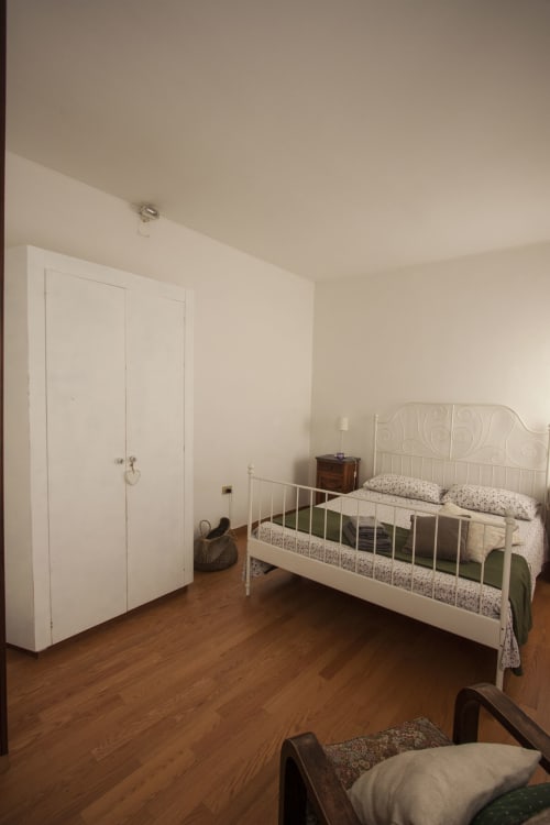 Bright bedroom in Ca Cortigiane Venice apartment with white iron bed, wardrobe, wooden floors