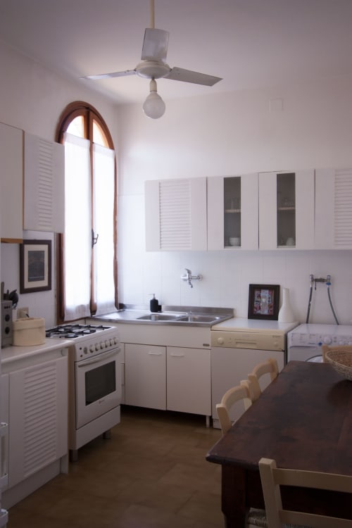Modern kitchen in Ca Cortigiane Venice apartment with white cabinets, gas stove, sink, and dining table