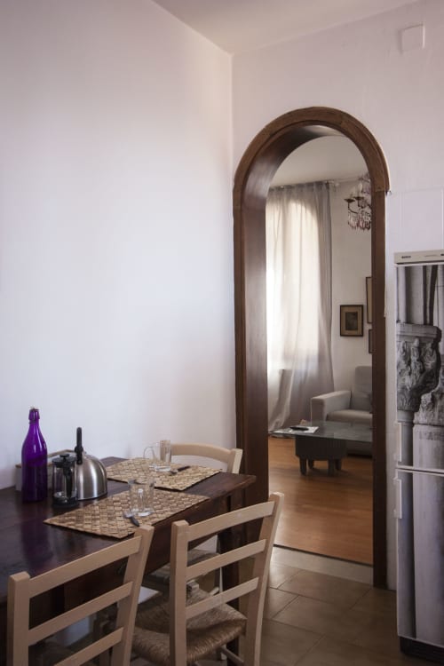 Dining area in Regina d'Oriente apartment, Venice, with wooden table, chairs, archway mirror, and kitchen appliances