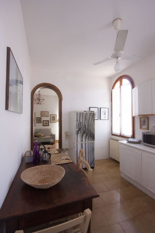 Bright kitchen-living area in Ca Cortigiane Venice apartment with dark wooden table, arched mirror, and white cabinetry