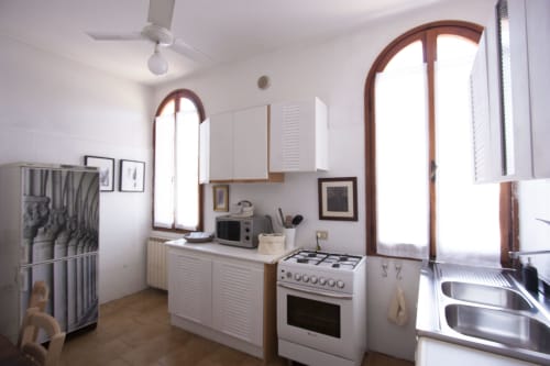 Bright kitchen in Ca Cortigiane's Regina d'Oriente apartment, Venice, with white cabinets, stove, and arched windows