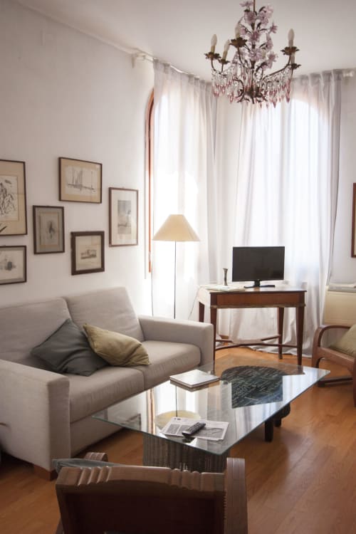 Elegante soggiorno dell'appartamento Ca Cortigiane a Venezia con divano, tavolino in vetro, lampadario e vista sulla città