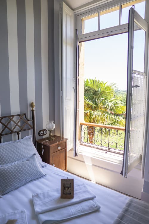 Sunny bedroom at La Venta de Miyares with striped walls, blue bedding, wooden furniture, and balcony views of palm trees