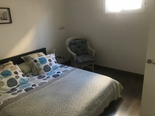 Habitación luminosa en Apartamentos Huelintown de Málaga con ropa de cama azul estampada, silla de mimbre y luz natural de la ventana