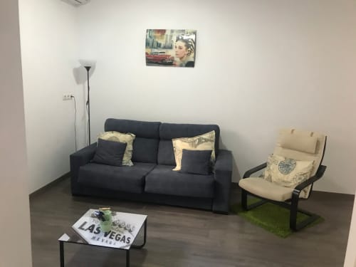 Sala de estar moderna en Apartamentos Huelintown, Málaga con sofá negro, butaca crema y decoración Las Vegas sobre madera oscura
