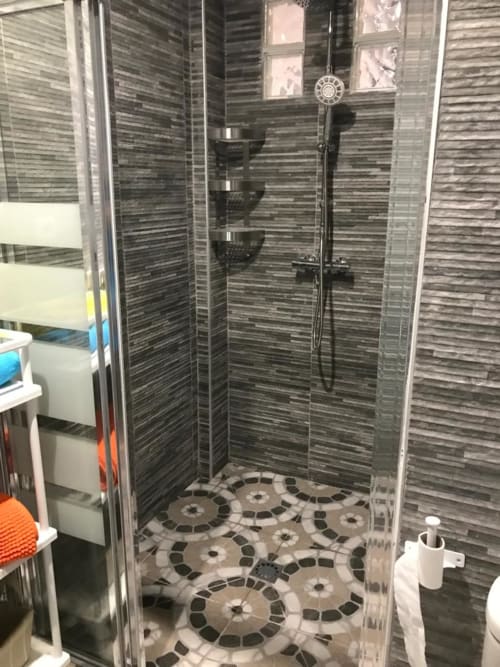 Moderno baño con azulejos horizontales oscuros y piso con patrón geométrico en Apartamentos Huelintown, Málaga