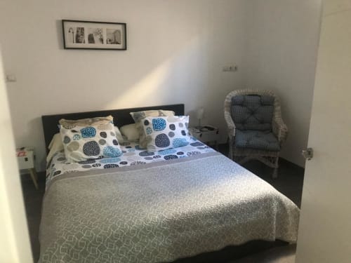 Dormitorio luminoso en Apartamentos Huelintown, Málaga con cama queen, ropa de cama geométrica azul, silla de mimbre y diseño moderno